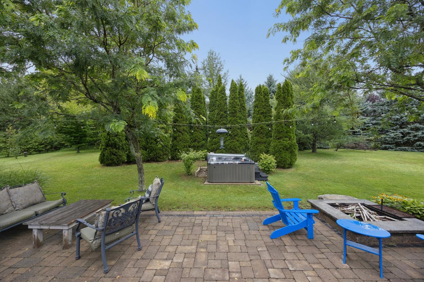 Stone patio with fire pit and hot tub amid mature trees at 30 Potters Lane